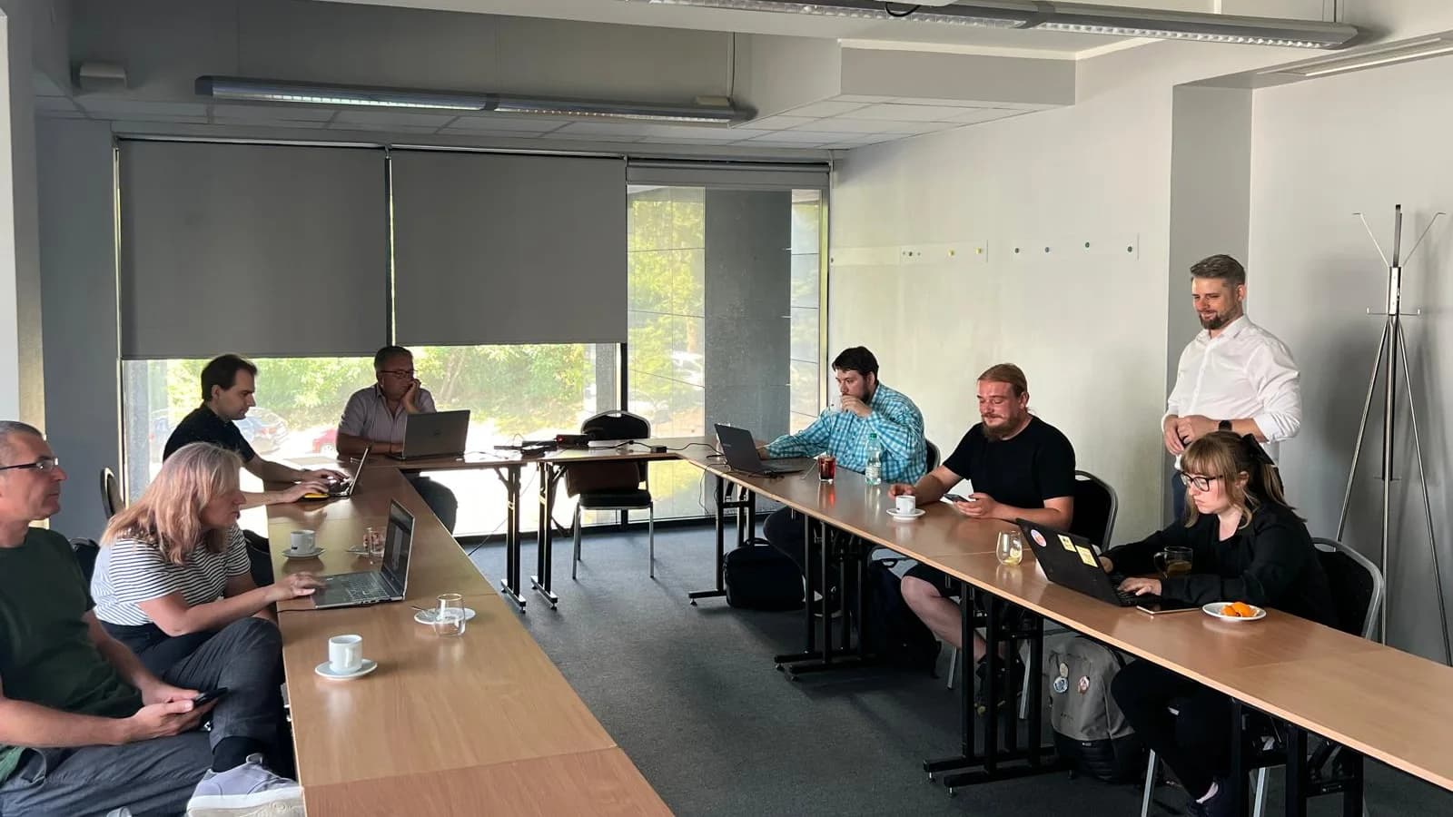 Uczestnicy warsztatów pracują przy laptopach w sali szkoleniowej, prowadzący stoi przy stole