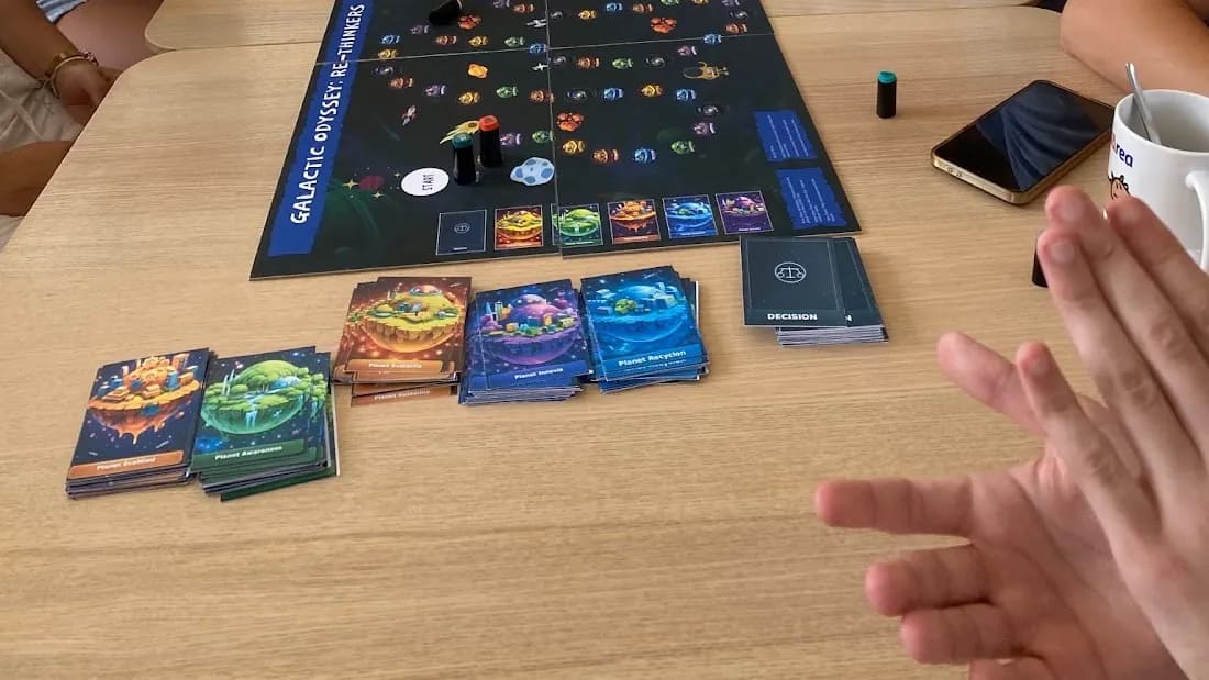 Plansza gry Galactic Odyssey: Re:Thinkers na stole, obok talie kart z planetami i talia kart decyzji